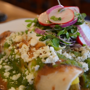 Two four tortila's filled with eggs and beans topped with salsa verde, black bean puree, sour cream, queso fresco, red onions, radishes and mixed micro green salad.